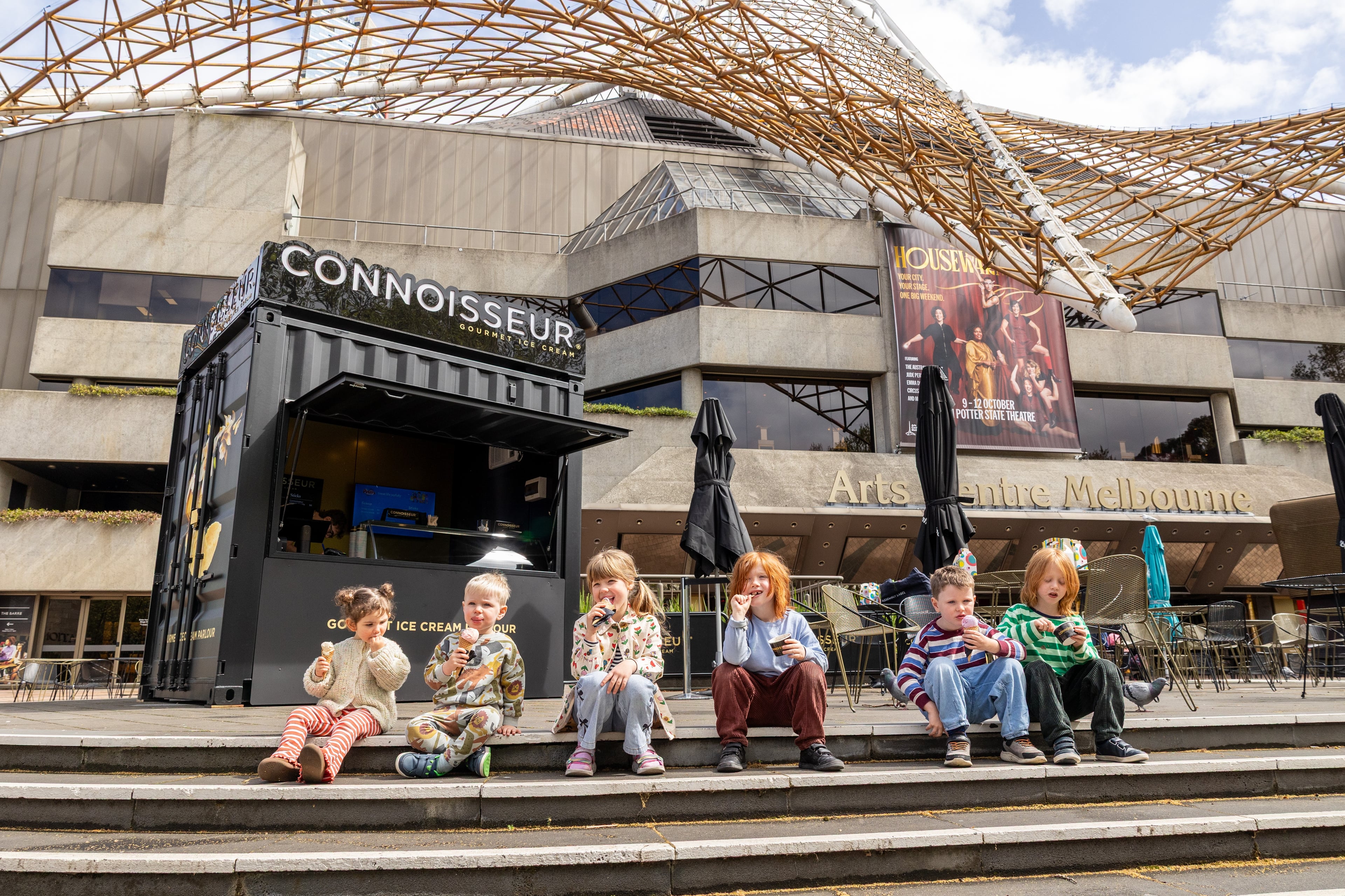 A group of children seated outside the Connoisseur ice cream stand at Arts Centre Melbourne.