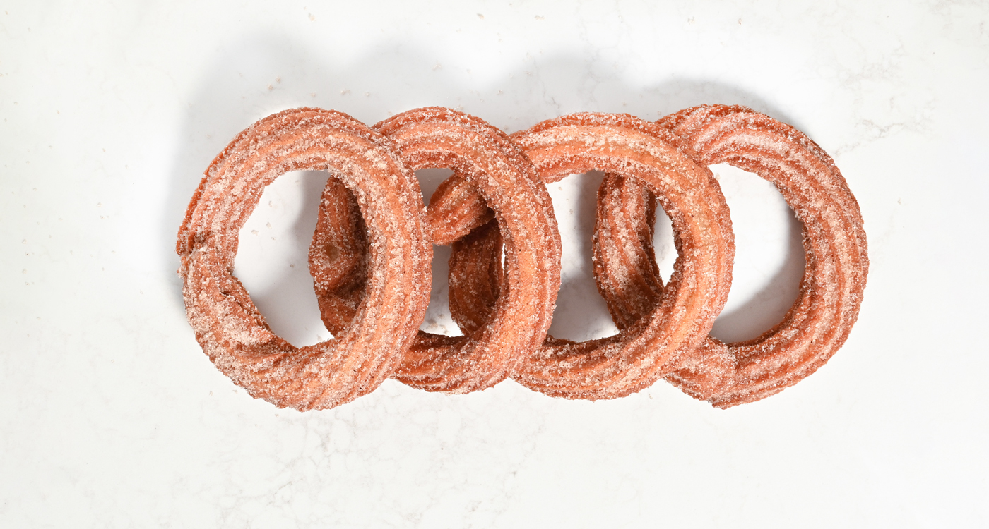 A flat lay style image of four Turkish donuts that are of a ring shape. They are stacked in line and are covered in sugar. 
