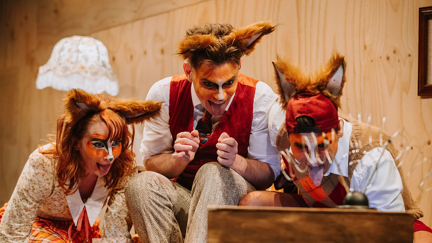Production image of Fantastic Mr Fox, depicted three actors dressed as foxes excitedly watching TV