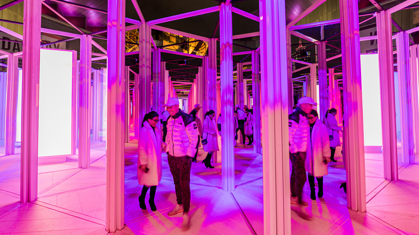A female and male walking through a mirror maze with fluro lights around them.
