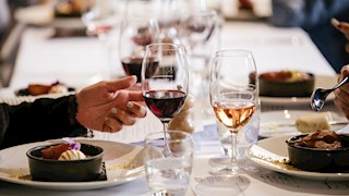 People sitting at table with white tablecloth, wine in wine glasses and plates of food.