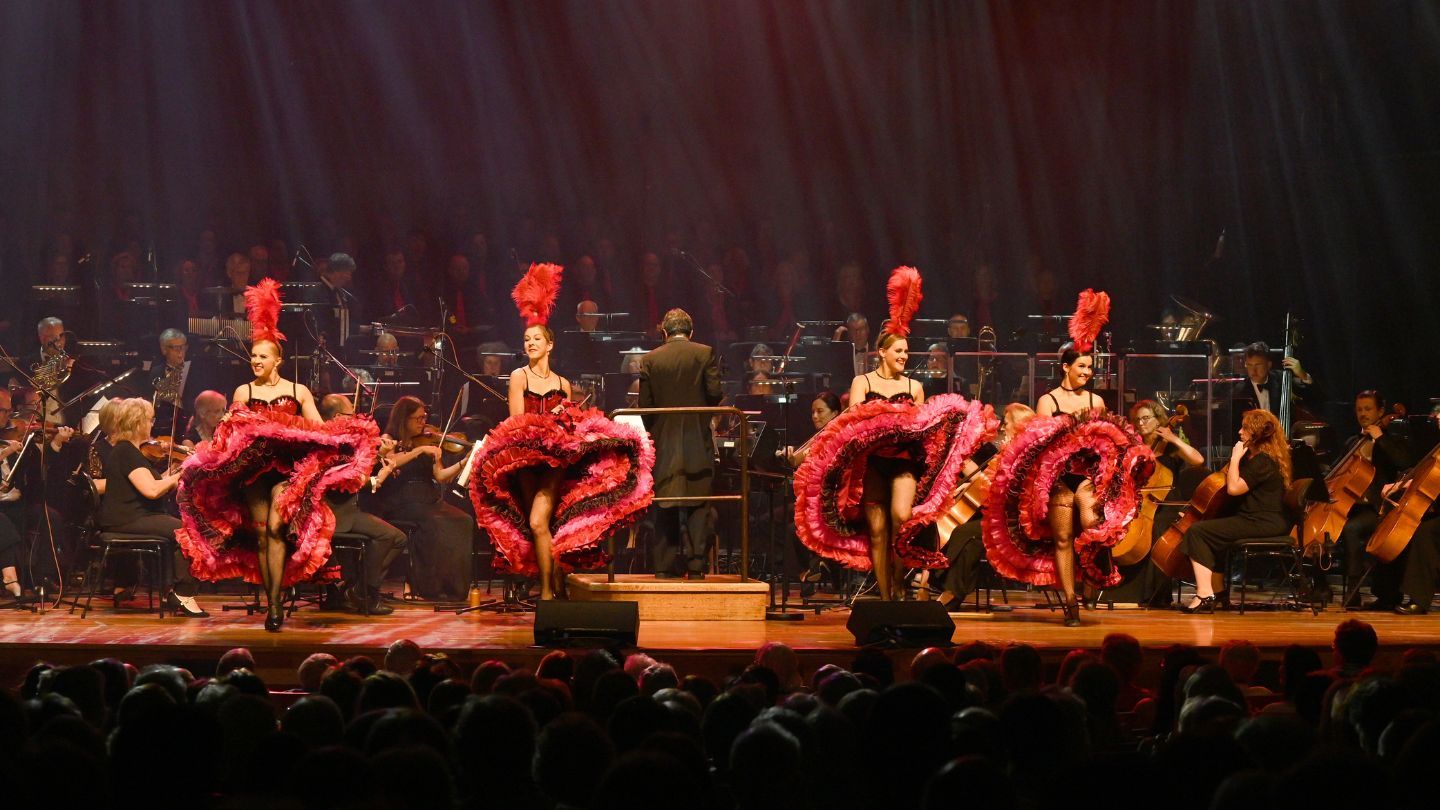 Four dancers on stage wearing large feathered skirts, and feathered head pieces.