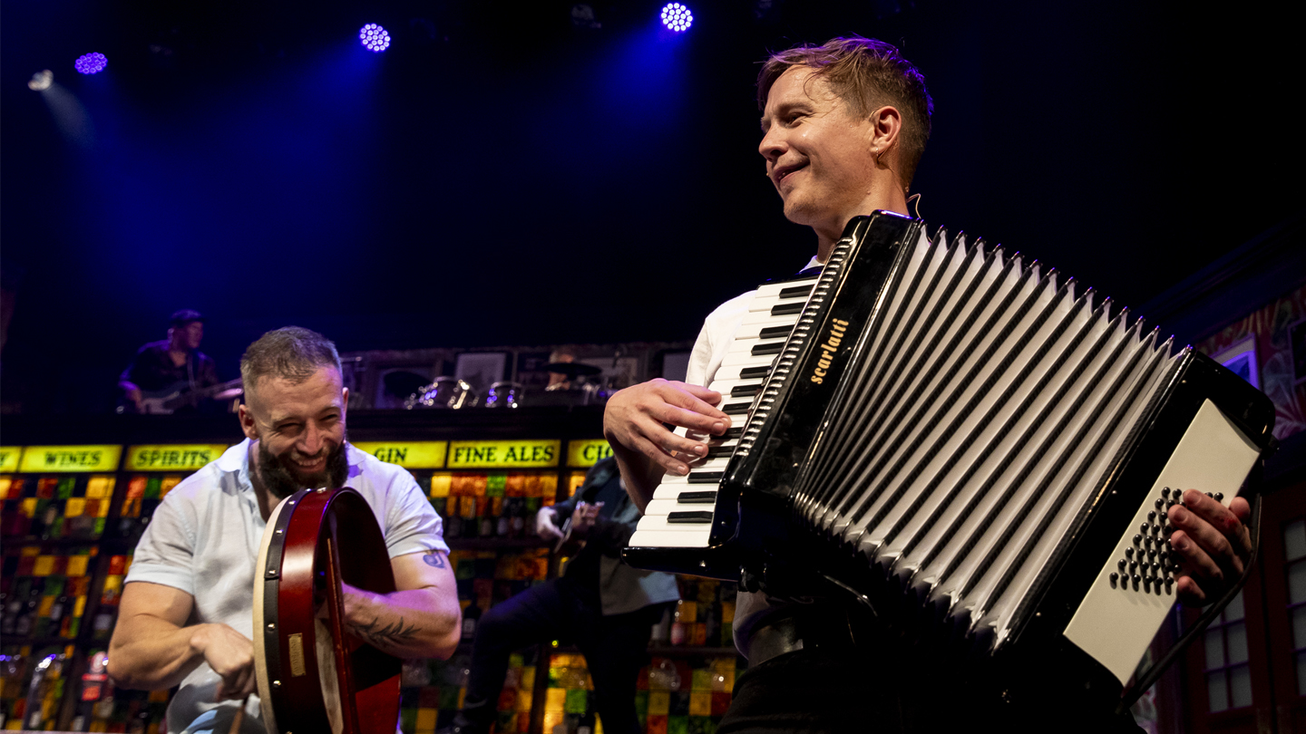 two men standing on stage smiling. they are both playing musical instruments. 