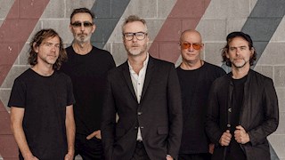 The National standing in front of a concrete wall. They are all wearing black.
