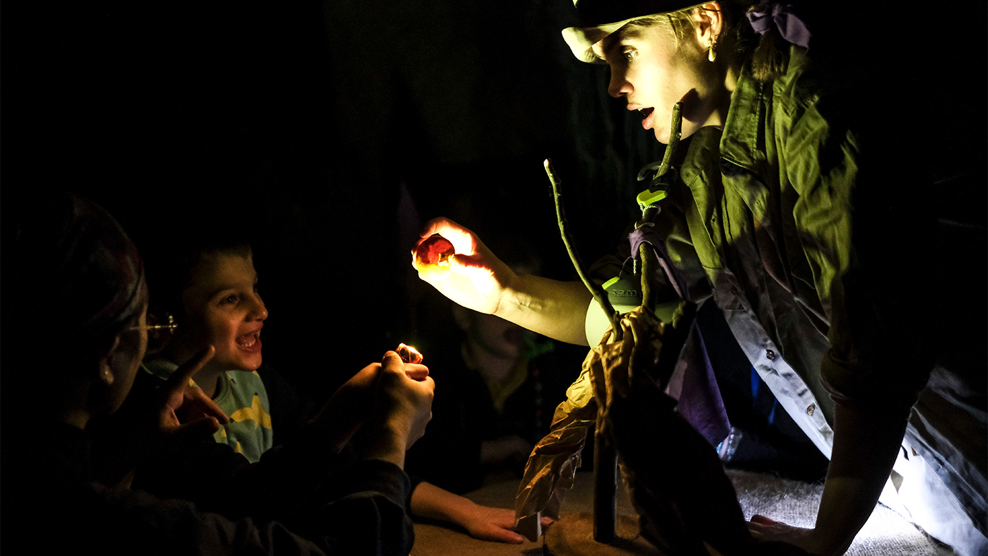 A young woman wearing a head lamp showing a couple of children something interesting.