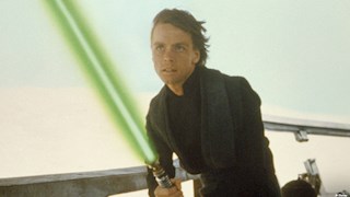 Mark Hamill as Luke Skywalker holding a green lightsaber. His hair is windswept and has a focused look on his face.