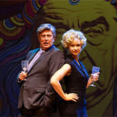 Two people dressed in formal attire standing back to back. They are each holding a champagne glass.