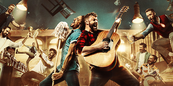 Men in an old pub drinking, dancing and singing. Two men are standing in the centre of the pub. one is holding a mop and singing into it like a microphone. the other man is singing and playing the guitar.